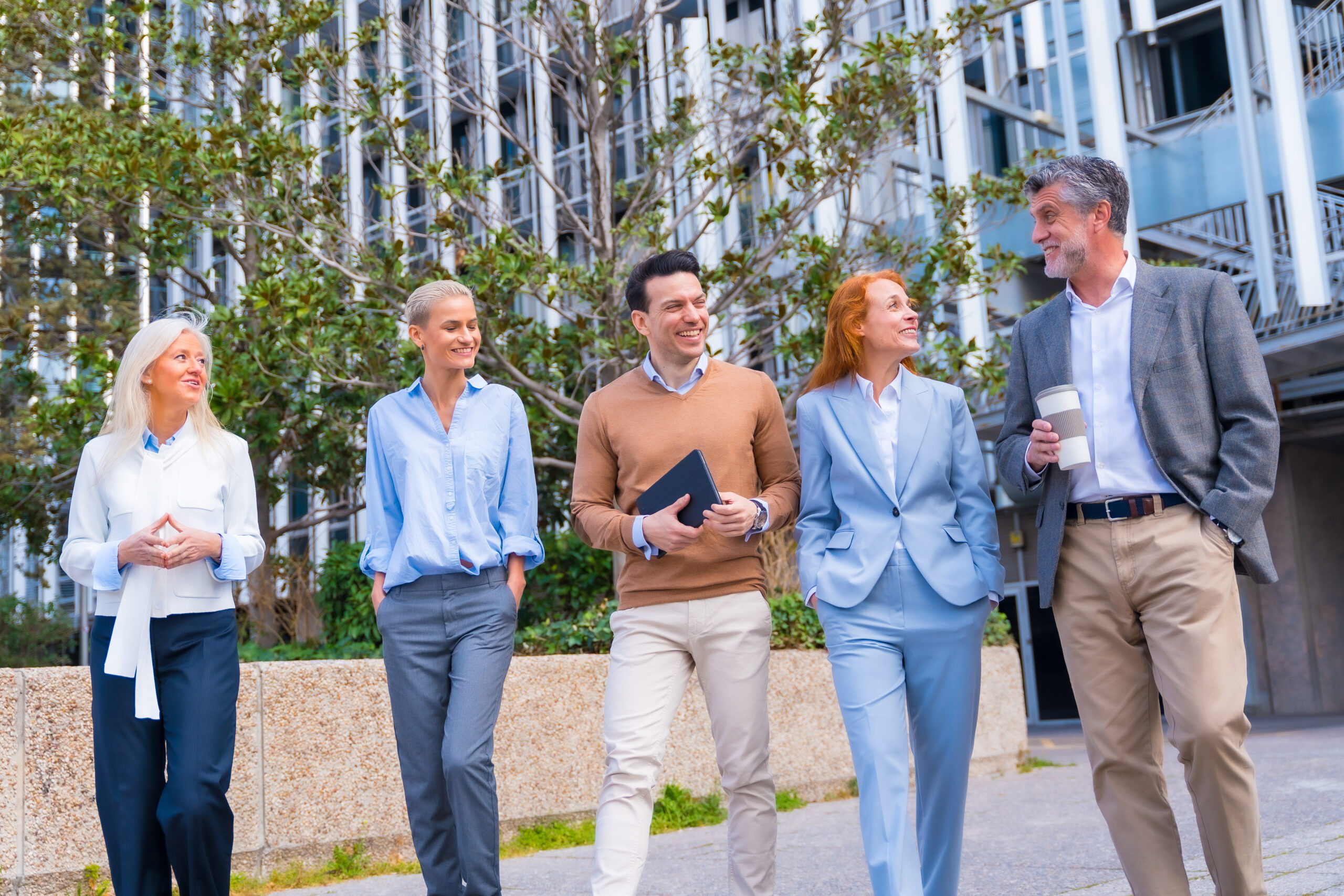 Group of coworkers walking going to work outdoors in a corporate office area, businesswoman and businessman and executives in commercial area